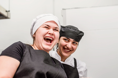 Two women chefs exchanging joyfully laughing in a kitchen